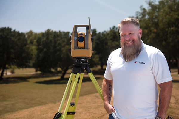 Shawn Collins standing next to a surveying theodolite. 